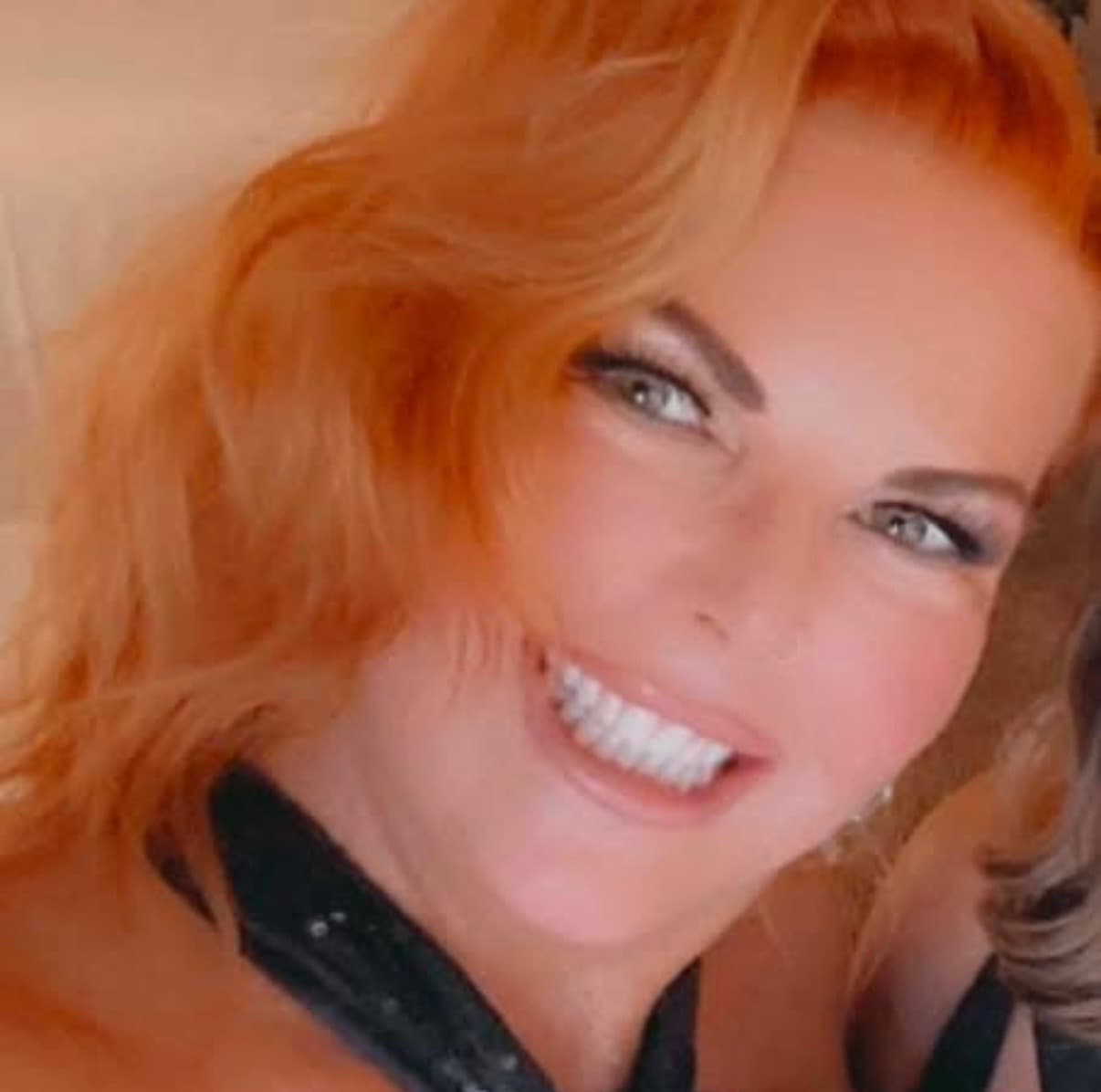 Smiling woman with vibrant orange hair, light eyes, and white teeth in a close-up.